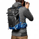 Rear-view of a photographer wearing the Lowepro PhotoSport BP 15L AW III backpack on a trail while lifting a camera to take a shot.