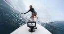 A surfer rides a wave with the waterproof DJI Action 6 camera mounted to their surfboard.