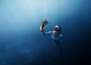 A scuba diver swimming underwater in deep blue water using the DJI Osmo Action 4 diving kit with a floating handle.