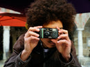 A man with curly hair taking a picture with a Fujifilm QuickSnap Black and White disposable camera, available at Best Camera Store.