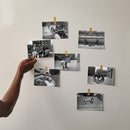 A hand placing black-and-white photographic prints captured with a Fujifilm QuickSnap camera on a wall, available at Best Camera Store.