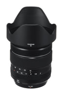High angle studio view of the Fujifilm Fujinon XF 16-80mm f-4 R OIS WR zoom lens standing vertically with its plastic petal lens hood attached