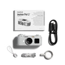 Fujifilm Instax Pal 2 digital camera shown with its retail box, black USB cable, white carrying strap, coiled cable, and magnetic strap clip on a clean white background.