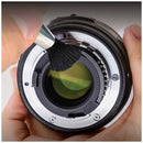 Close-up demonstration of the soft-bristled Optex lens brush gently removing dust from the rear element glass mount of a camera lens.