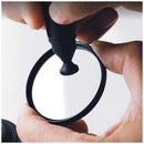 Detailed close-up of a photographer using the circular carbon cleaning tip of the Optex precision lens pen to clear smudges from a protective glass lens filter.
