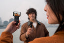 Person holding a smartphone recording another person outdoors with a cityscape in the background