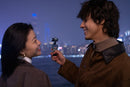 Two people standing close together with a cityscape in the background at night.