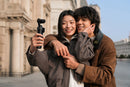 Two people hugging outdoors with a  Insta360 luna pocket  camera stabilizer, surrounded by classical architecture.