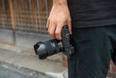 Hands holding the Tamron 16-50mm f/2.8 lens with lens hood 2 attached to a Sony mirrorless camera from Best Camera Store.