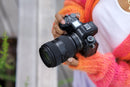 A photographer holding a Nikon Z camera equipped with the compact Tamron 35-100mm f/2.8 zoom lens for travel and portraiture.
